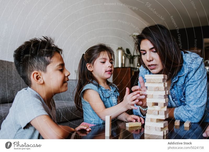 Junge ethnische Mutter mit Kindern spielt Turmspiel zu Hause Frau spielen Konzentration Zusammensein Freizeit Strategie unterhalten Brettspiel genießen Liebe