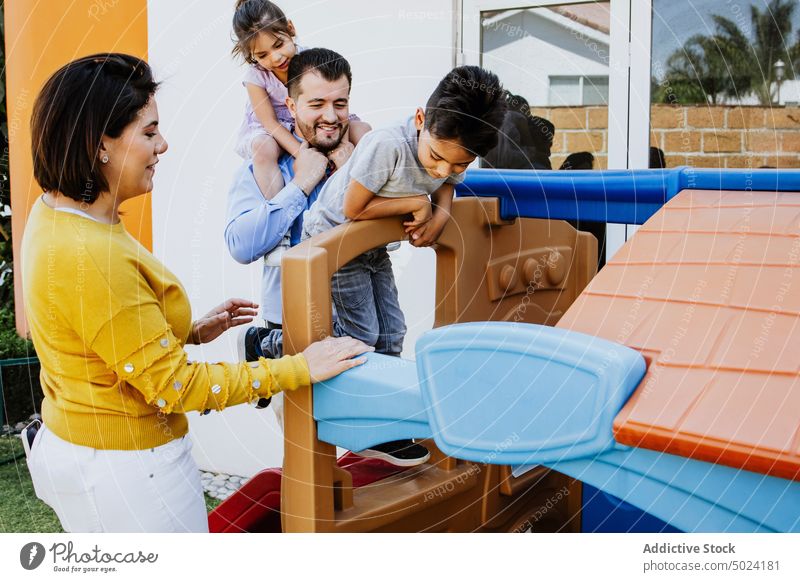 Fröhliche ethnische Familie spielt auf Rutschen auf dem Spielplatz spielen Hinterhof Mutter Vater Kinder Zusammensein Freude Glück Zeit verbringen Kindheit