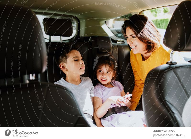 Ethnische Mutter schnallt ihr kleines Mädchen mit dem Smartphone im Auto an Frau Kind befestigen Gurt PKW Sicherheit Tochter Fahrzeug Passagier Automobil