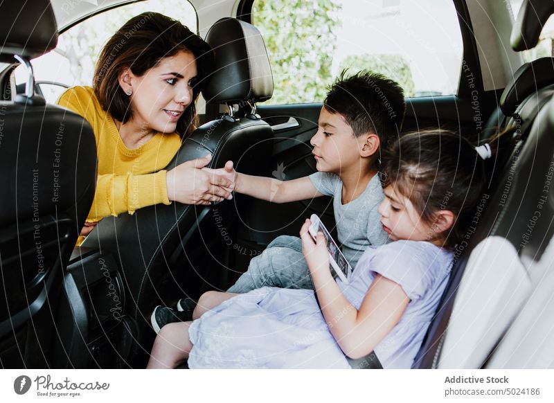 Kleine ethnische Geschwister benutzen ihr Smartphone auf dem Rücksitz eines Autos und unterhalten sich mit ihrer Mutter Frau Kinder PKW Zusammensein Talkrunde