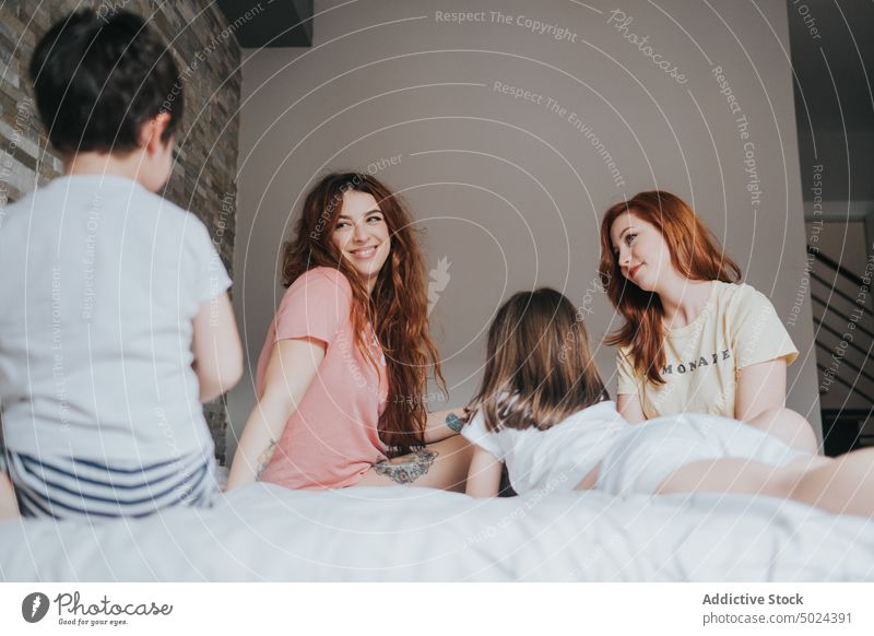 Lächelnde Frauen auf dem Bett sitzend mit Kindern im Innenbereich Schlafzimmer alternativ heiter Kindheit Komfort gemütlich heimisch Freundschaft von unten Spaß
