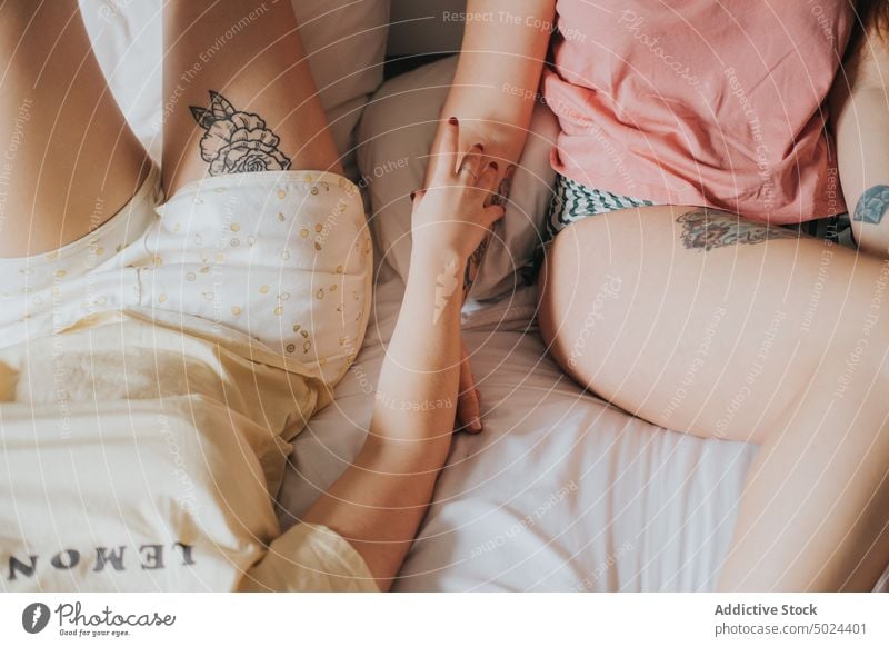 Frauen mit Tattoos auf dem Bett liegend im Innenbereich jung Schlafzimmer alternativ anonym Kunst Streu Komfort Paar gemütlich Ernte gesichtslos Freund