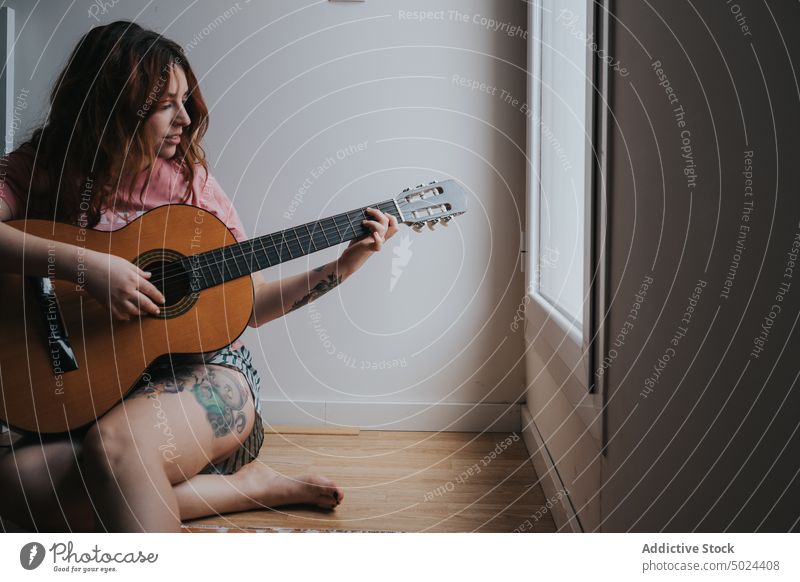 Junge lächelnde Frau mit Gitarre, die zu Hause sitzt Musik im Innenbereich Instrument akustisch attraktiv schön Dunkelheit heimisch heimwärts Lachen LAZY