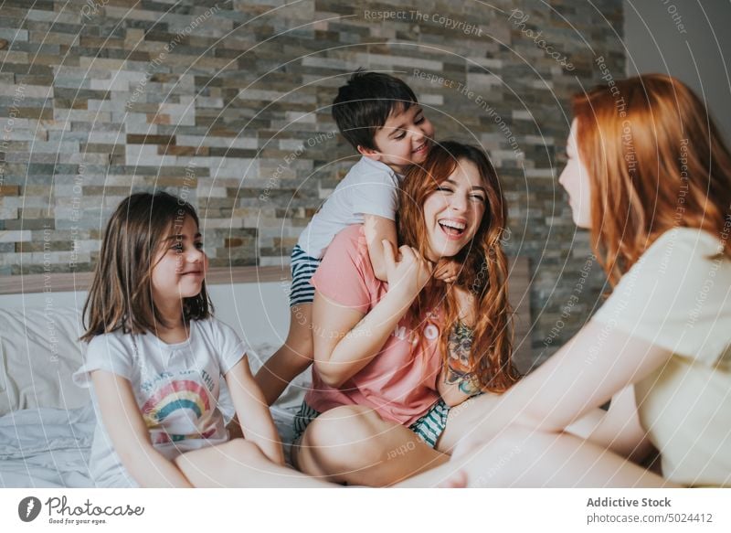 Lächelnde Frauen auf dem Bett sitzend mit Kindern Freundschaft Spaß im Innenbereich Lachen Freizeit alternativ Schlafzimmer heiter Kindheit Komfort gemütlich