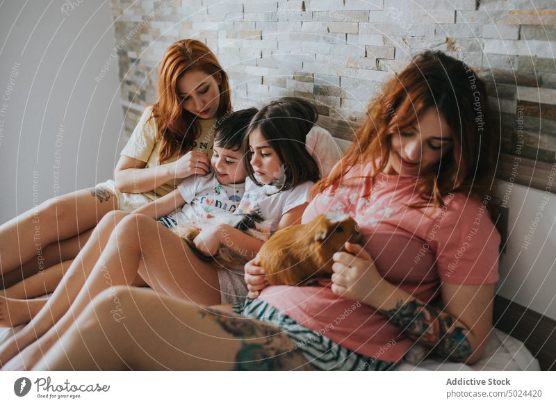 Frauen und Kinder mit Meerschweinchen auf dem Bett liegend Familie im Innenbereich Schlafzimmer Fröhlichkeit Tier Pflege heiter Komfort bequem gemütlich