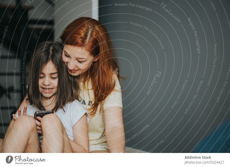 Frau umarmt Mädchen mit Smartphone auf dem Bett im Innenbereich Liebe Kind Rücken Schlafzimmer Browsen brünett Pflege Kindheit Komfort Textfreiraum gemütlich