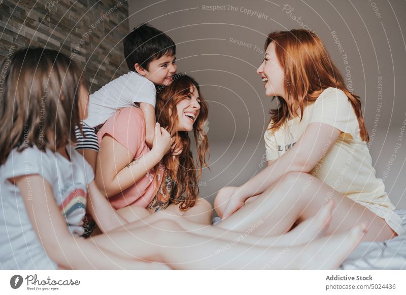 Lächelnde Frauen auf dem Bett sitzend mit Kindern im Innenbereich Spaß Freundschaft alternativ Schlafzimmer heiter Kindheit Komfort gemütlich heimisch von unten