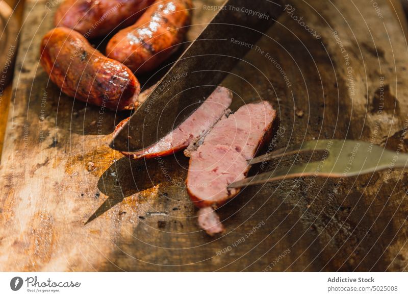 Messer über leckerer gegrillter Wurst auf Schneidebrett Wurstwaren Schweinefleisch Fleisch Ernährung Protein Lebensmittel geschnitten Fleischgabel Utensil