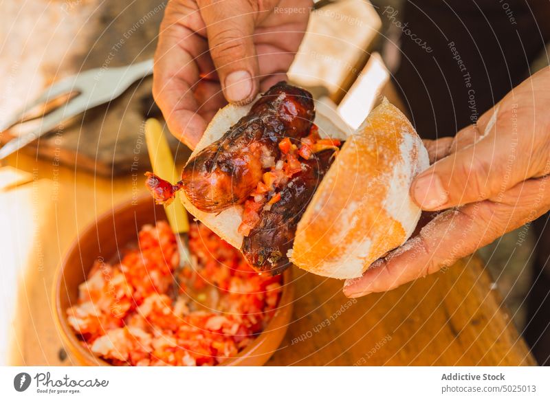 Ein Mann bereitet ein Sandwich mit Wurst und gehacktem Gemüse vor vorbereiten Belegtes Brot Wurstwaren Mittagessen Bohnenkraut geschmackvoll gegrillt