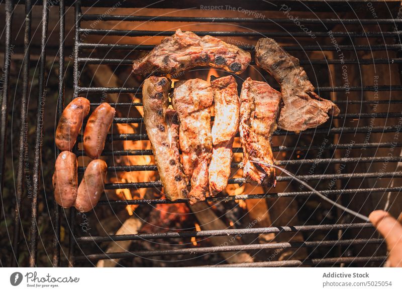 Crop-Person, die leckere Fleischstücke über dem Feuer grillt Wurstwaren Grillrost Barbecue Lebensmittel Protein Ernährung Ablage Aroma Spielfigur