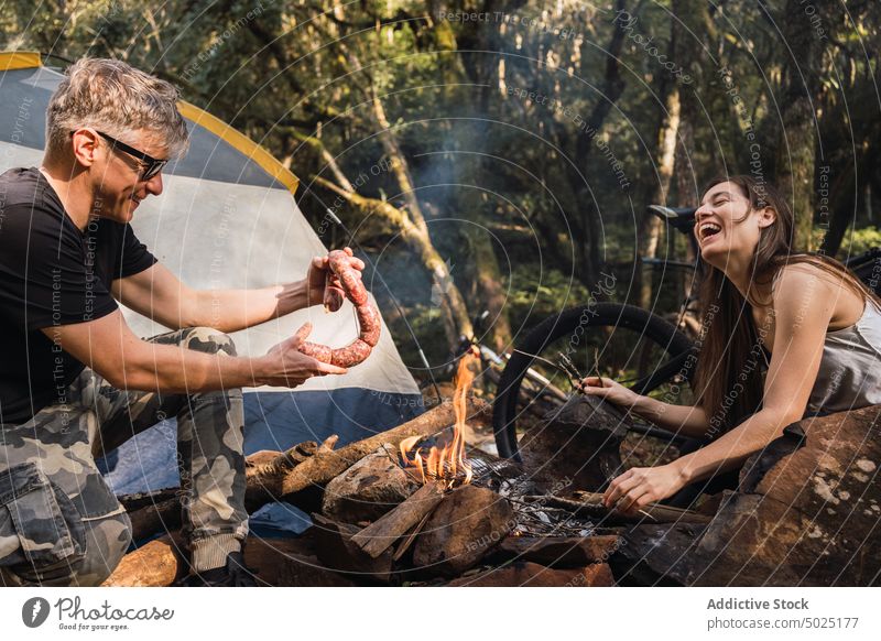 Wanderer legt frische Würste auf den Rost über dem brennenden Feuer vorbereiten Wurstwaren Barbecue Grillrost Rindfleisch Brandwunde Campingplatz Mann natürlich