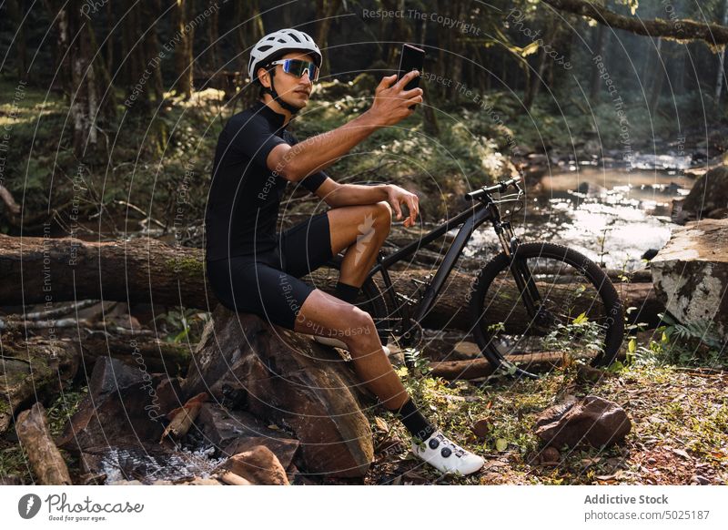 Unbekannter Radfahrer fotografiert mit Smartphone im Wald einen Fluss fotografieren Natur Sport Ausflug Mann benutzend Apparatur Bach Fahrrad Umwelt Schutzhelm