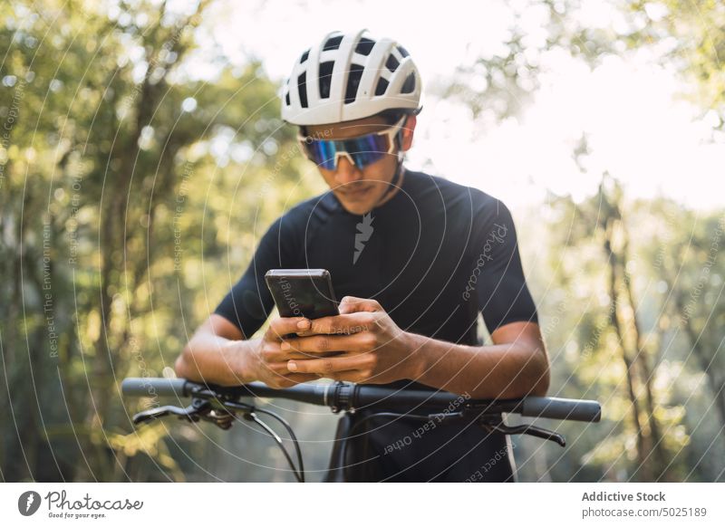 Radfahrer auf dem Fahrrad plaudert im Wald mit seinem Smartphone plaudernd Internet online Sport Zyklus Mann Wälder benutzend Apparatur kreativ Design