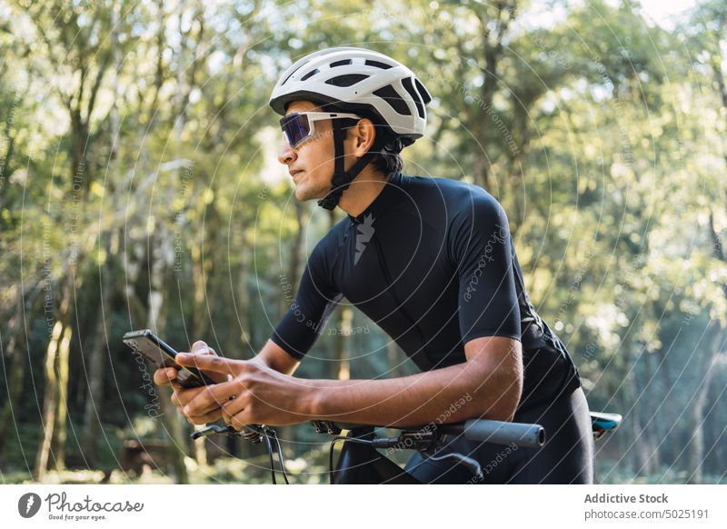 Radfahrer auf dem Fahrrad plaudert im Wald mit seinem Smartphone plaudernd Internet online Sport Zyklus Mann Wälder benutzend Apparatur kreativ Design