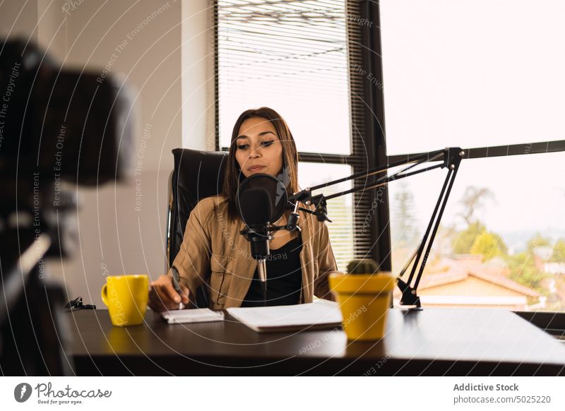Frau im Radiosender schreibt auf einen Notizblock Wirt Kopfhörer Mikrofon zur Kenntnis nehmen Notebook Ausstrahlung Blog Schreibstift schreiben Aufzeichnen