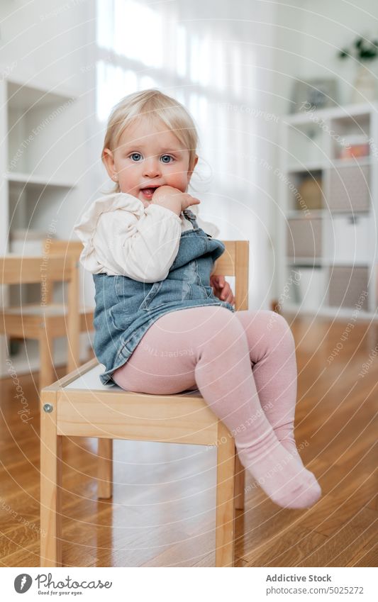 Adorable Kleinkind Mädchen auf Stuhl im Haus Kindheit neugierig achtsam unschuldig süß heimwärts Porträt eng Jeansstoff gesamt Kleid sitzen Parkett charmant