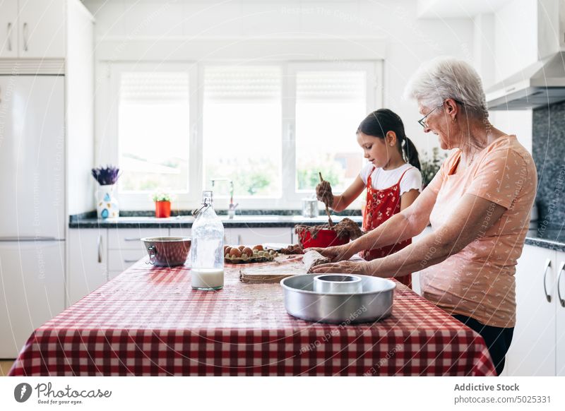 Lächelnde Großmutter mit Mädchen bei der Zubereitung von Teig zu Hause Enkelin Teigwaren Koch kulinarisch Rezept heiter Zeit verbringen Küche selbstgemacht Frau