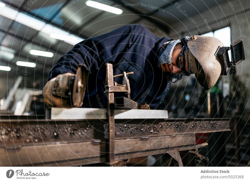 Brutaler Schweißer bei der Arbeit in einer schmutzigen Garage Schweißnaht Maschine Mann Metallbearbeitung Werkstatt Schutzhelm Handschuh männlich behüten