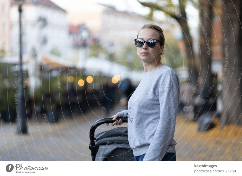 Stilvolle junge Frau mit Sonnenbrille zu Fuß durch Ljubljana Stadtzentrum schieben und schaukelnden Kinderwagen. Warmes Herbst- oder Frühlingswetter für Aktivitäten im Freien