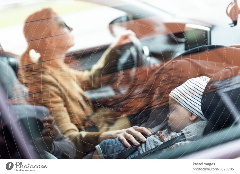 Eine Mutter, die sich auf das Fahren des Familienautos konzentriert, um Besorgungen zu machen, während ihr Baby in der Babyschale an ihrer Seite schläft. PKW