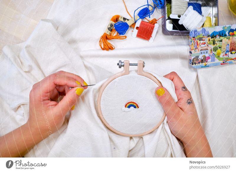 Stickerei eines Regenbogens auf ein T-Shirt. Frau Hand Tattoo Sticken Kleidung Baimwolle kunst Handarbeit Kunsthandwerk Reifen Werkstoff Nadel Näharbeit