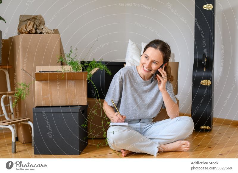 Fröhliche Frau, die während eines Umzugs mit ihrem Smartphone spricht sprechen schreiben Hinweis verlegen Kasten Lächeln Hausbesitzerin Glück einziehen