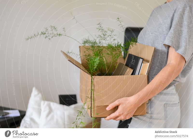 Crop-Frau, die eine Schachtel mit Habseligkeiten trägt führen Kasten Zugehörigkeit verlegen Buch Pflanze eingetopft heimwärts lässig Appartement einziehen