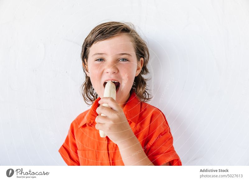 Liebenswertes hungriges Kind isst Banane vor weißem Hintergrund Mädchen essen Frucht Lächeln Glück gesunde Ernährung positiv Porträt heiter Lebensmittel lecker