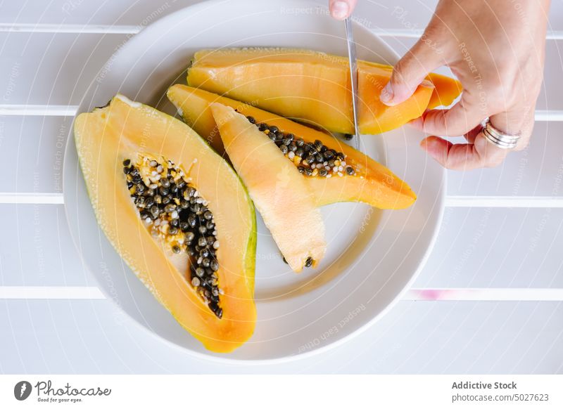 Anonyme Person, die eine Papaya mit einem Messer schneidet geschnitten Frucht Lebensmittel Vitamin exotisch frisch tropisch lecker reif ganz Teller Hand