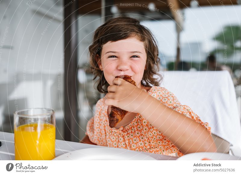 Glückliches Kind beißt in ein leckeres Croissant in der Cafeteria Mädchen essen Kantine Biss Café Frühstück Ernährung nähren Orangensaft Glas Lebensmittel