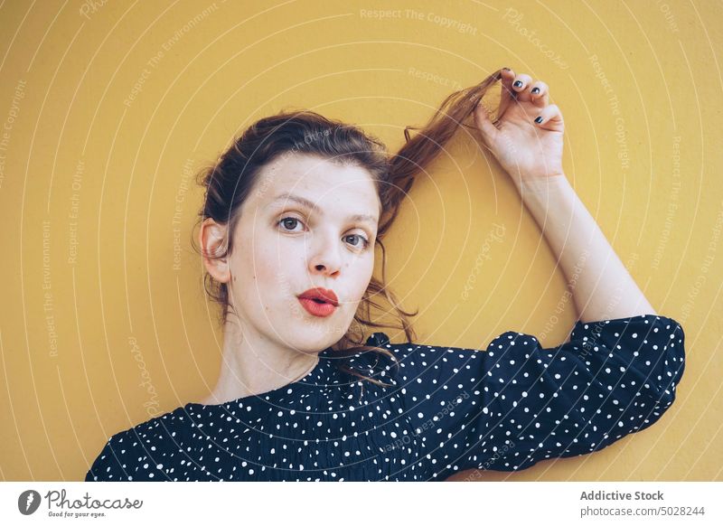Selbstbewusste Frau, die ihr Haar im gelben Studio berührt selbstsicher Haare berühren Kokette Stil heiter Porträt Freude jung brünett rote Lippen Kleid Flirten