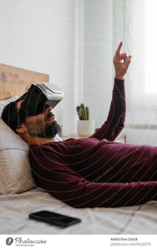 Mann interagiert mit virtueller Realität auf dem Bett Virtuelle Realität VR Punkt Hochtechnologie Schutzbrille Headset erkunden interagieren Lügen Schlafzimmer