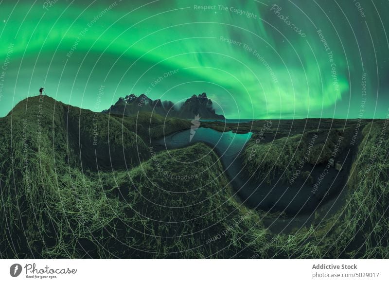 Anonymer Fotograf unter dem Himmel mit Polarlichtern in der Nähe des Sees stehend Reisender Fotoapparat Nordlicht Berge u. Gebirge Winter fotografieren Nacht