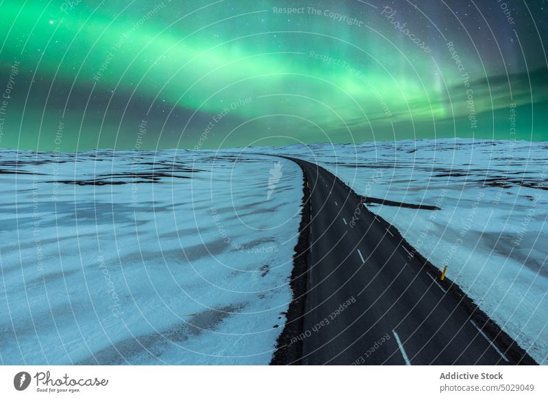 Leere Asphaltstraße inmitten eines schneebedeckten Feldes unter einem Himmel mit Nordlicht Straße nördlich Licht Winter Landschaft Nacht polar Aurora Island