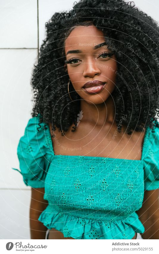 Ernste afroamerikanische Frau, die in der Nähe einer weißen Wand steht emotionslos Model Stil Vorschein Top türkis Afro-Look Make-up lässig Frisur Outfit