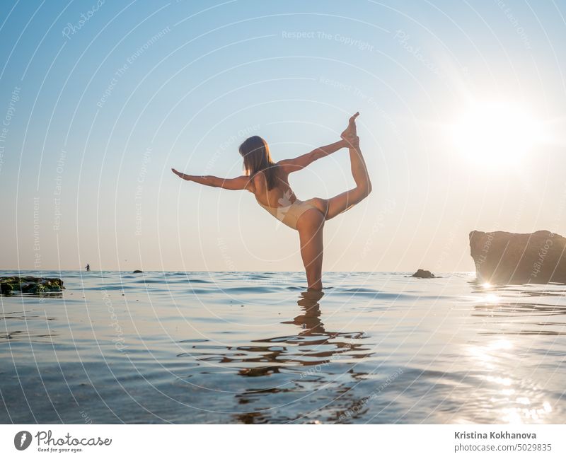 junge Frau im Badeanzug übt Yoga auf erstaunliche Sonnenaufgang. Fitness, Sport, Yoga und gesunder Lebensstil Konzept. Mädchen tun exersices im Meerwasser Natur