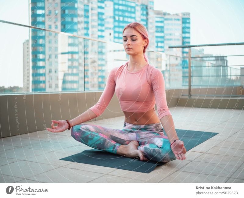 Junge schöne Frau in rosa Trainingsanzug meditiert während Outdoor-Training auf Wolkenkratzer Terrasse, sie fühlt sich Frieden in megalopolis. Sportliches Mädchen macht Yoga auf dem Dach.