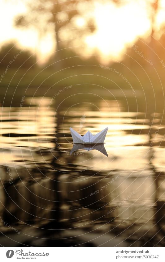 Ein Papierboot schwimmt auf den Wellen im Wasser bei einem schönen Sonnenuntergang. Origami Schiff Segeln. Das Konzept eines Traums, Zukunft, Kindheit, Freiheit oder Hoffnung.
