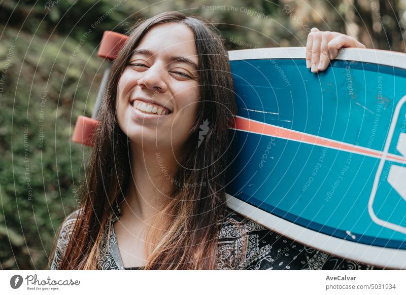 Junge Frau posiert und lächelt mit einem Skateboard Longboarding im Wald, Gen Z Sportaktivitäten Teenager Lächeln Person Porträt jung Natur schön Einstellung