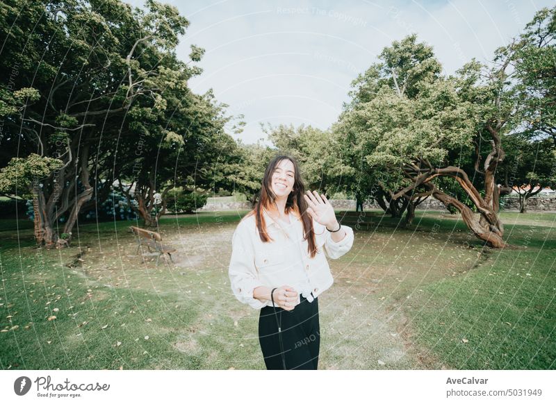 Porträt einer jungen Frau, die an einem sonnigen Tag im Park in die Kamera grüßt, Weitwinkelobjektivbild Person Gruß Lächeln stylisch Jugend Glück sorgenfrei