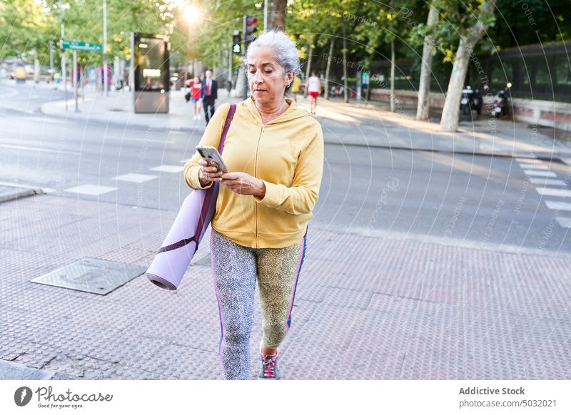 Ältere Sportlerin, die auf der Straße läuft und ihr Smartphone benutzt Spaziergang benutzend Training Fitness soziale Netzwerke Bürgersteig online Frau Senior