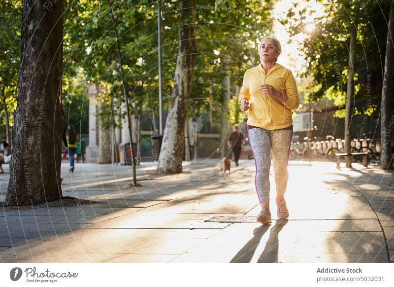 Ältere Sportlerin läuft auf der Straße laufen Sonnenaufgang Herz Fitness Training Straßenbelag Morgen Übung Frau Wellness Wohlbefinden atmen Energie Aktivität