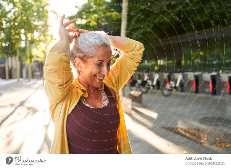 Glückliche ältere Sportlerin beim Frisieren Lächeln Pferdeschwanz Krawatte Fitness Training Straße Morgen vorbereiten Frau gealtert Senior Vitalität Athlet