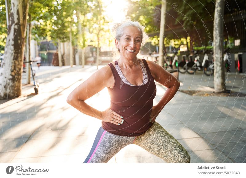 Lächelnde ältere Sportlerin beim Training auf der Straße Athlet Übung Fitness Park Ausfallschritt außerhalb Wohlbefinden sportlich Gesundheit Sportbekleidung