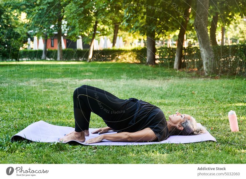 Ältere Frau macht Brücke Pose im Park Yoga Sitzung Rasen Unterlage Brückenstellung üben Sommer Zen älter Senior gealtert Asana Vitalität Wellness Wohlbefinden