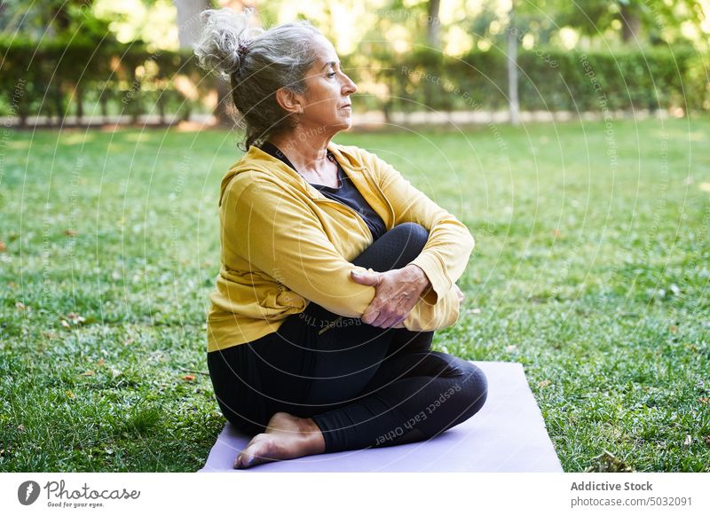Ältere Frau dehnt sich während einer Yoga-Sitzung Dehnung Park verdrehen Sommer Unterlage Asana Windstille älter Senior gealtert üben Energie