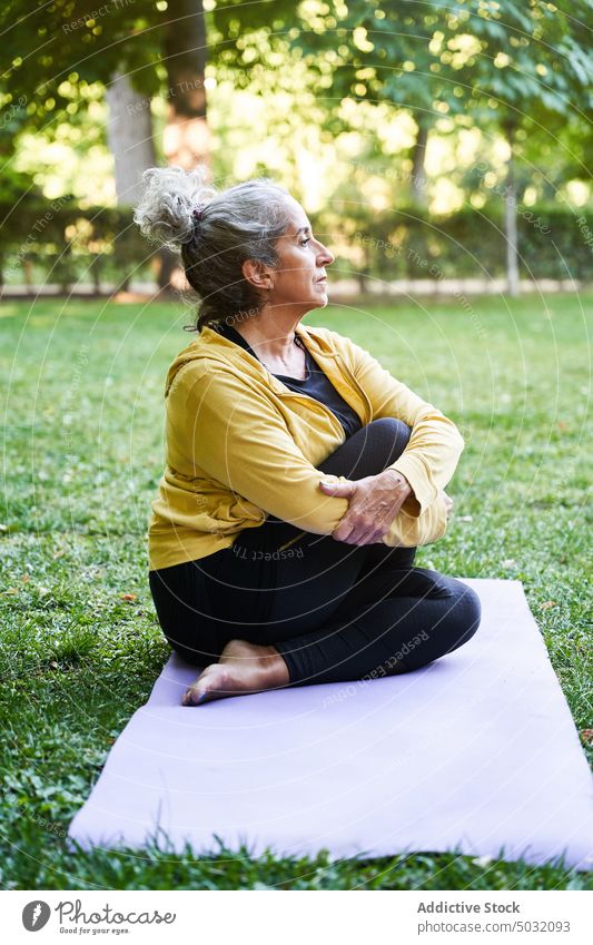 Ältere Frau dehnt sich während einer Yoga-Sitzung Dehnung Park verdrehen Sommer Unterlage Asana Windstille älter Senior gealtert üben Energie