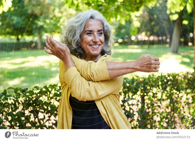 Glückliche ältere Sportlerin, die ihre Schulter dehnt Dehnung Fitness Training Park Lächeln Übung Sommer physisch Frau Senior gealtert Vitalität Aktivität
