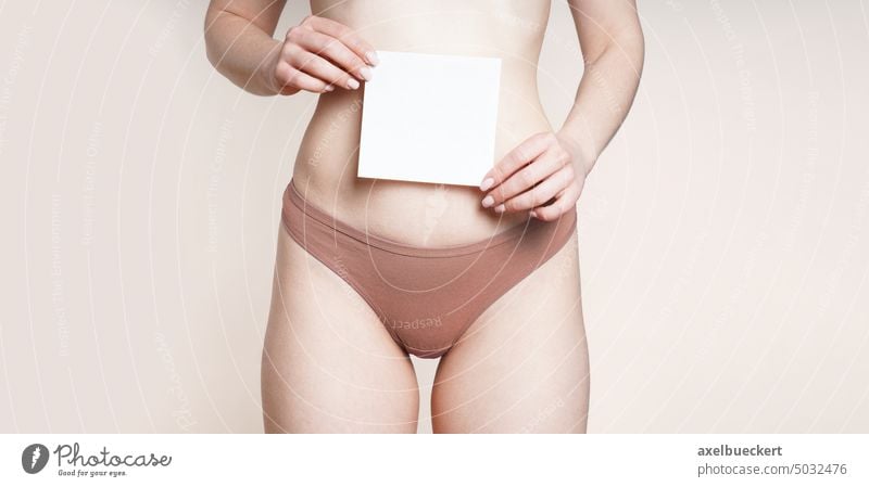 Frau in Unterwäsche hält ein leeres Blatt Papier über den Bauch Frauenunterhose Gesundheit der Frauen Magen Gynäkologie Sexualität Zeichen Textfreiraum