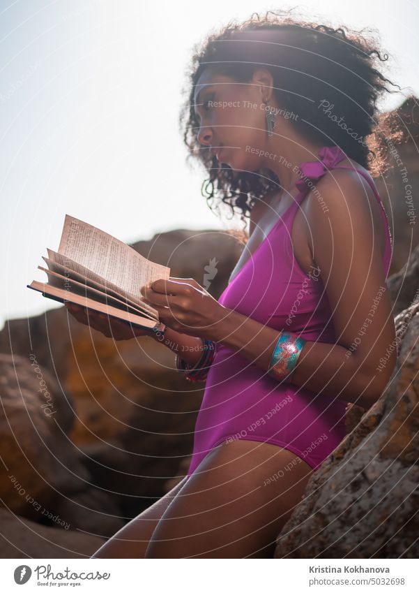 Schöne afrikanische Frau liest Buch auf den Felsen Strand, hübsche schwarze Frau genießt Sommerurlaub entspannend im Freien jung schön Freizeit